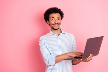 Young stylish man with curly hair holding laptop against a vibrant pink background, smiling confidently