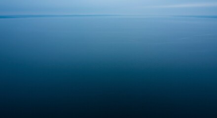 Obraz premium Serene expanse of deep blue water stretching to the horizon under a hazy sky