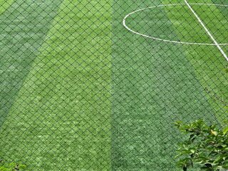 Looking through the net, you can see soccer field covered with green grass. Football field is...