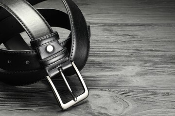 One black leather belt on wooden table, closeup. Space for text