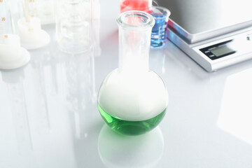 Flask with green liquid, other laboratory glassware and scale on white mirror table, closeup