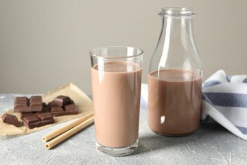 Tasty chocolate milk in glass, bottle and pieces on grey table