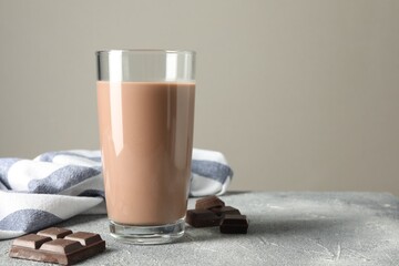 Tasty chocolate milk in glass and pieces on grey table, closeup. Space for text