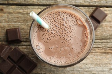 Tasty chocolate milk in glass and pieces on wooden table, flat lay