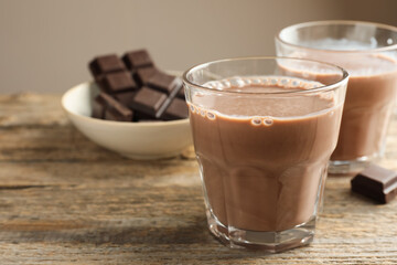 Tasty chocolate milk in glasses and pieces on wooden table, closeup. Space for text
