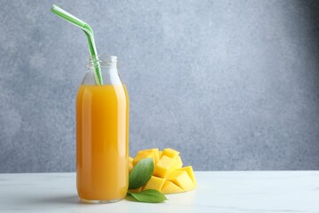 Tasty mango juice in glass bottle, fresh fruit and green leaves on white marble table, space for text