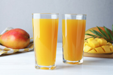 Tasty mango juice in glasses, fresh fruits and green leaves on white wooden table, closeup