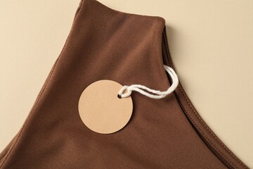 Brown garment with tag on beige background, top view