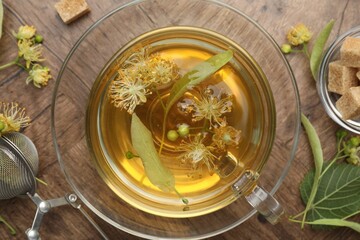 Fresh linden tea in cup, sugar cubes and flowers on wooden table, flat lay