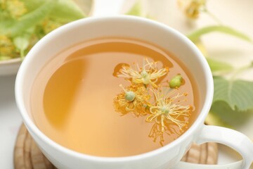 Fresh linden tea in cup and flowers on white table, closeup