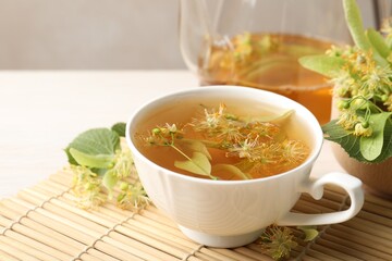 Fresh linden tea in cup, teapot and flowers on white table, closeup. Space for text
