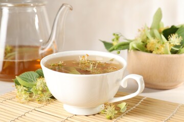 Fresh linden tea in cup, teapot and flowers on white table, closeup