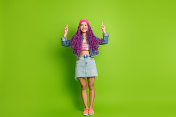 Smiling young woman wearing stylish denim outfit on vibrant green background showcasing gestures...