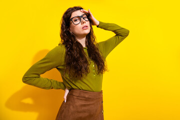 Stylish young woman wearing glasses and casual green shirt on bright yellow background striking a thoughtful pose