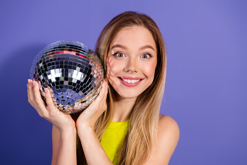 Young woman holding a sparkling disco ball on a vibrant purple background, smiling brightly and...