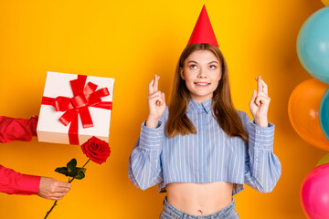 Young woman in festive casual outfit crossing fingers in anticipation with balloons and gift...
