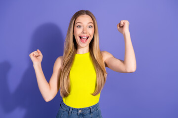 Fototapeta premium Optimistic young woman cheering actively in casual yellow top against vibrant purple backdrop showcasing joyful energy