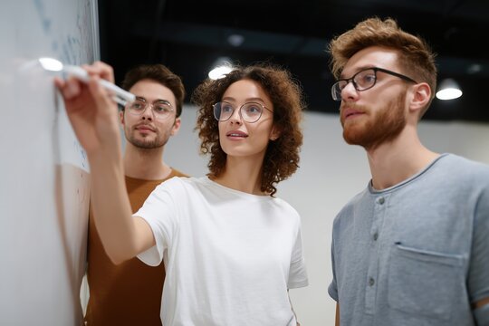 A trio of focused colleagues collaborate, brainstorming ideas and insights, leveraging the whiteboard for visual communication, showcasing teamwork and innovation.