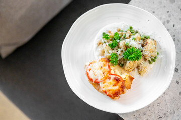 Baked chicken breast topped with cheese and tomato, served with cauliflower, peas, and parsley on a white plate. Healthy homemade meal, photographed close-up.