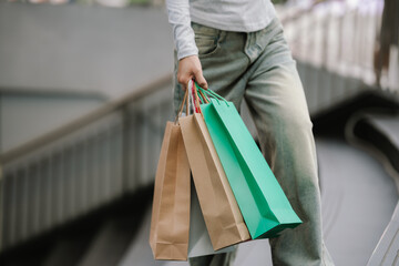 A person in jeans and a long-sleeved shirt carries several colorful shopping bags, likely after a...