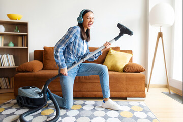 Cleaning is fun. Joyous woman listening to music in headphones while vacuuming her apartment, using...