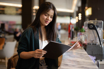 Fototapeta premium young woman reading menu in restaurant bar