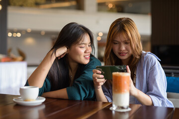 two women drinking coffee in cafe and using mobile phone