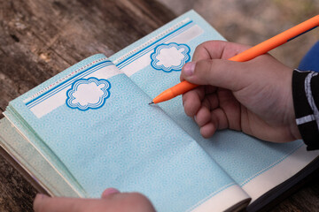 A child writes in a vintage diary with blue pages using an orange pen