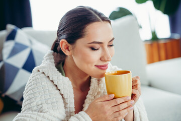 Young woman enjoying a relaxing moment with a hot drink at home wrapped in a blanket, feeling cozy and happy