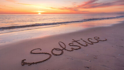  Solstice word written in wet sand, serene beach sunset or sunrise on the background.