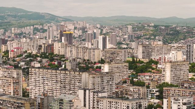 Tbilisi cityscape with Soviet blocks and modern buildings against green hills and mountains