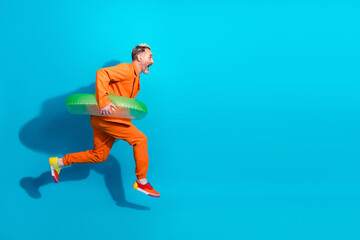 Stylish middle-aged man in vibrant orange outfit posing with a green inflatable against a blue...