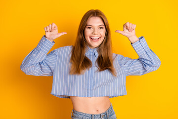 Cheerful young woman in casual outfit pointing at herself with enthusiasm in front of a bright...