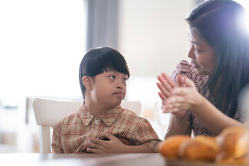 A child with Down syndrome playing ukulele while mother claps along, encouraging musical...