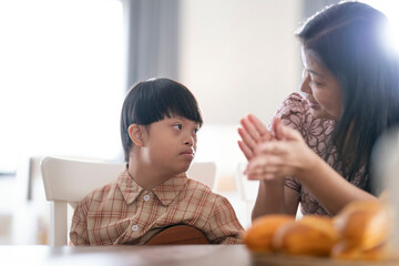 A child with Down syndrome playing ukulele while mother claps along, encouraging musical...