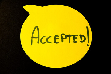 Photograph of a yellow emoji on a black background with the word "accepted"written inside.