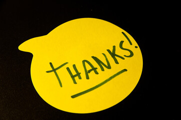 Photograph of a yellow emoji on a black background with this word "Thanks" written inside.
