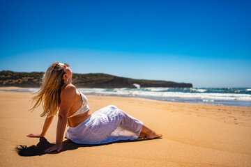 Beautiful middle aged woman sitting on seashore and sunbathing on sandy beach Bordeira Praia in...