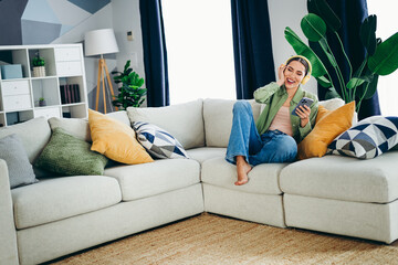 Obraz premium Adorable woman enjoying music at home, sitting on a comfortable sofa with a smartphone