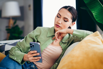 Young woman relaxing on a sofa at home while using her smartphone in a comfortable and stylish...
