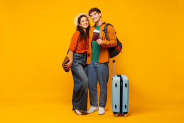 Happy spouses ready for vacation, posing with travel tickets and luggage suitcase, posing over...