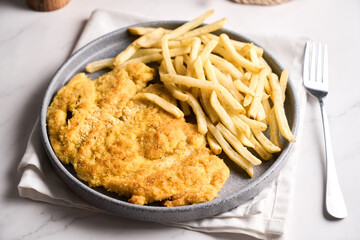 Pork or chicken Milanese, with french frieson plate on wooden table. Mediterranean, latin american food.
