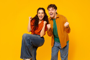Obraz premium Wow, yes. Overjoyed couple shaking clenched fists, cheering and looking at camera, posing over orange background wall