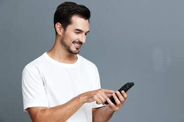 Smiling man in casual white t-shirt interacts with smartphone, expressing happiness while standing...