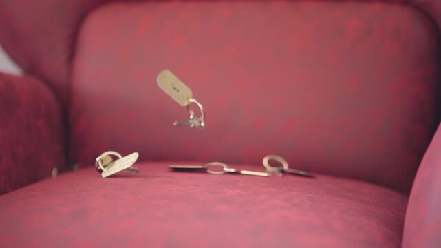 Set of hotel keys is captured mid air falling and bouncing onto a red sofa, slow motion