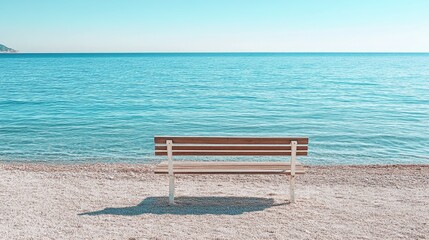 A solitary wooden bench sits on a tranquil, pebble beach overlooking a calm, azure sea under a clear, bright sky