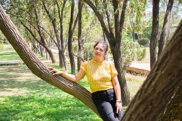 Beautiful young Indian Lady wore black jeans and yellow top posing with tree in the garden during her holiday. travel, fashion, lifestyle concept