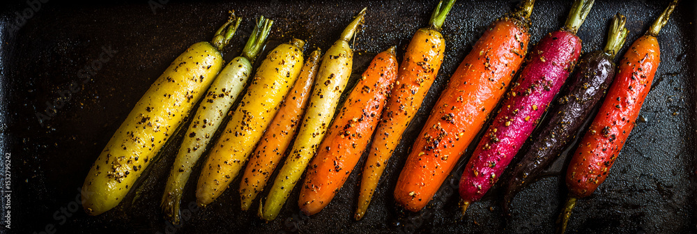 Poster a vibrant array of roasted carrots in various colors arranged on a dark baking sheet close up view