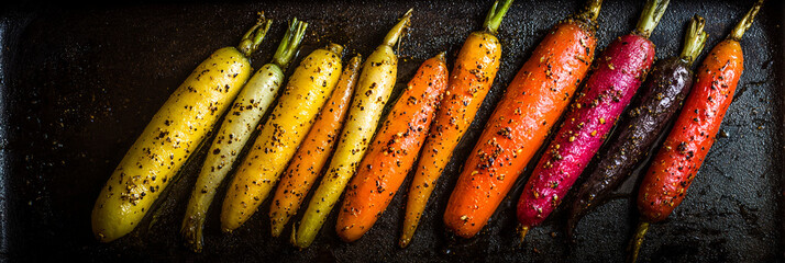 A vibrant array of roasted carrots in various colors arranged on a dark baking sheet close up view