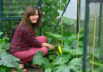 A woman smiling beside a ripe yellow zucchini, in June, 2025. 